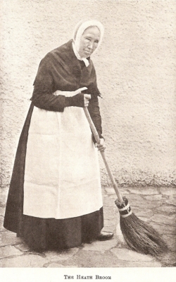 Elderly English woman in white pinafore holding broom
